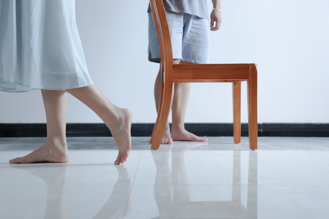 Dve osoby s bosými nohami v bielej miestnosti so stoličkou