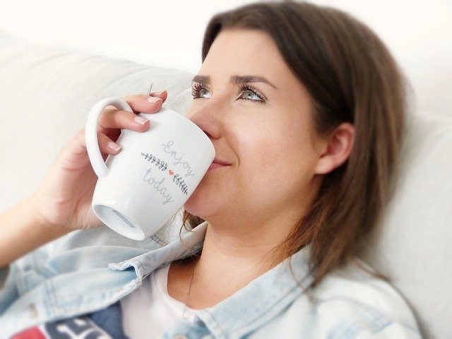 Žena leží v posteli a pije čaj z bielej šálky.jpg